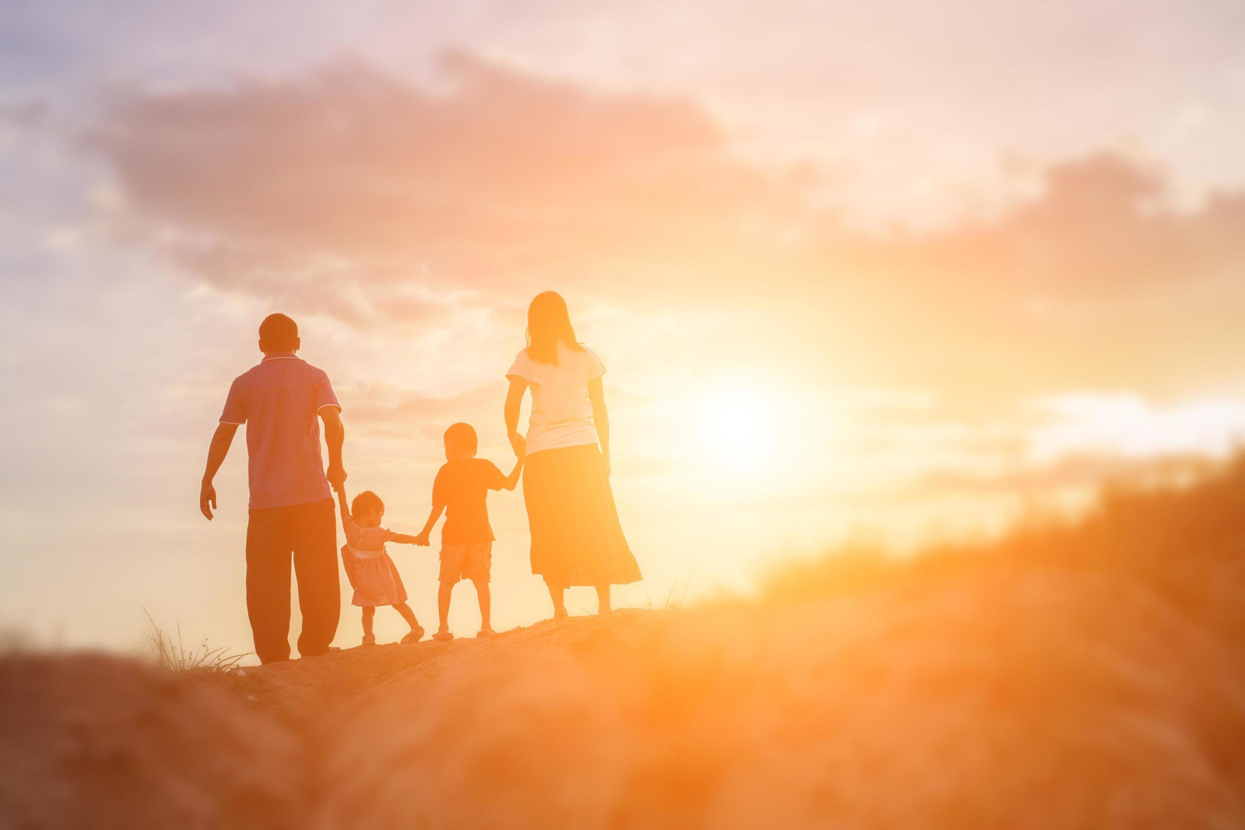 family of four standing holding hands at dawn